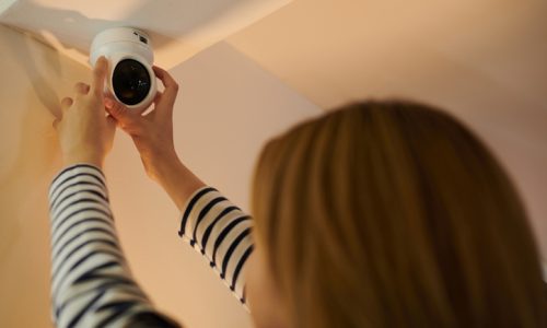 Woman installing security camera on ceiling in apartment